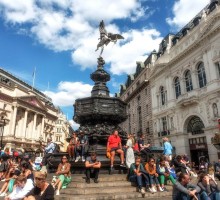 Tourists sitting on the steps of the Shaftesbury Memorial Fountain and statue of Greek god Anteros, Piccadilly Circus, London’s West End.